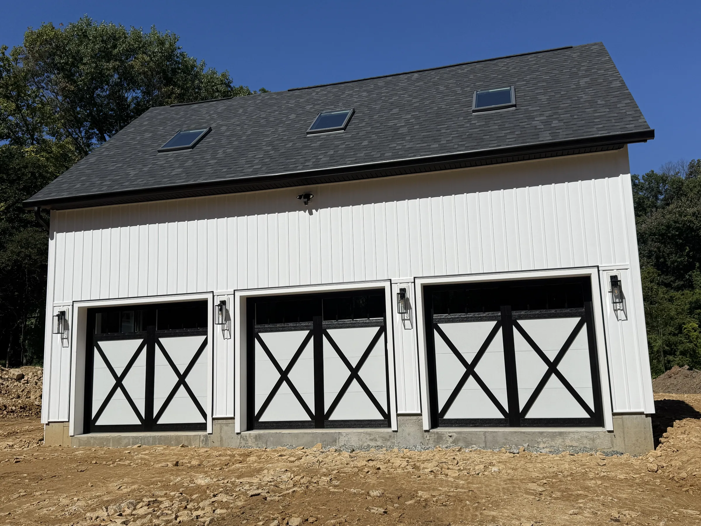 Three white carriage-style garage doors with black X-brace trim and upper windows installed on a detached residential garage.
