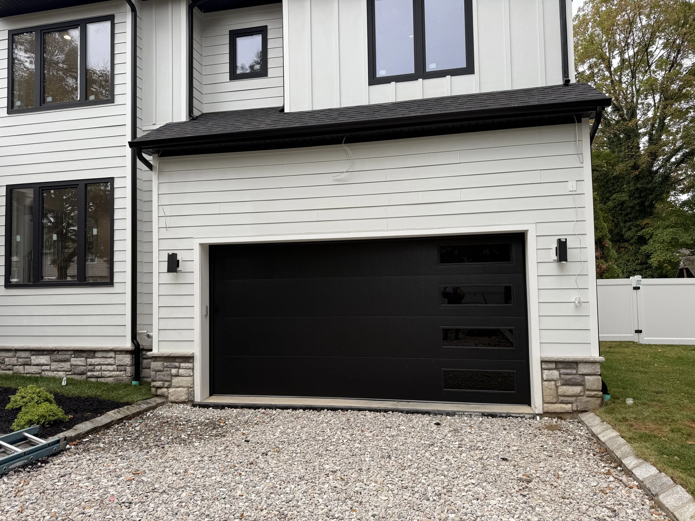 Wide black modern garage door with horizontal side windows installed on a white residential exterior.
