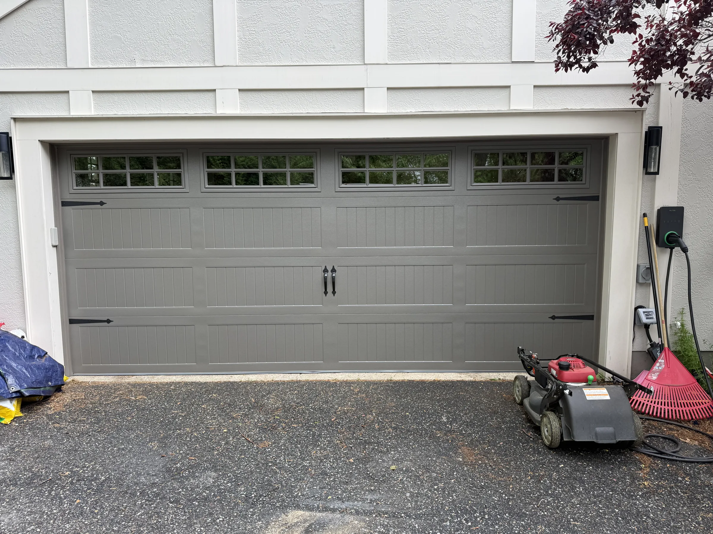 Gray traditional garage door with upper windows and black decorative hardware installed on a white residential home.