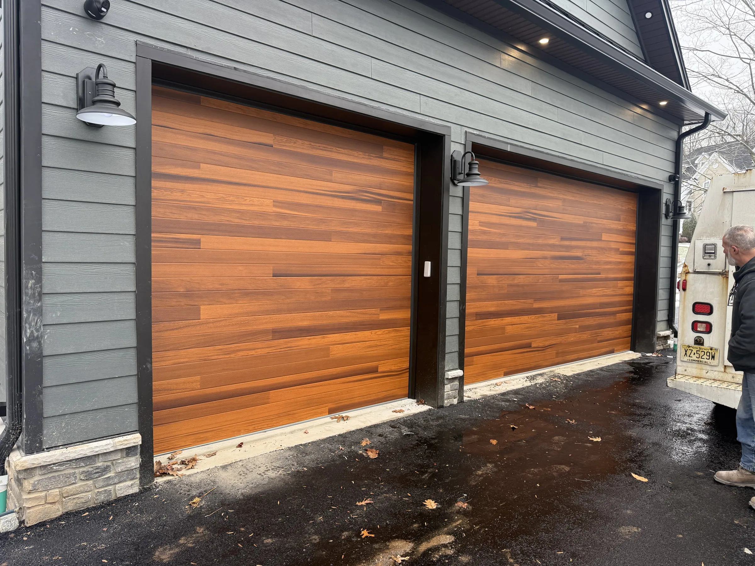 Pair of flush wood-look garage doors installed on a dark gray residential exterior.