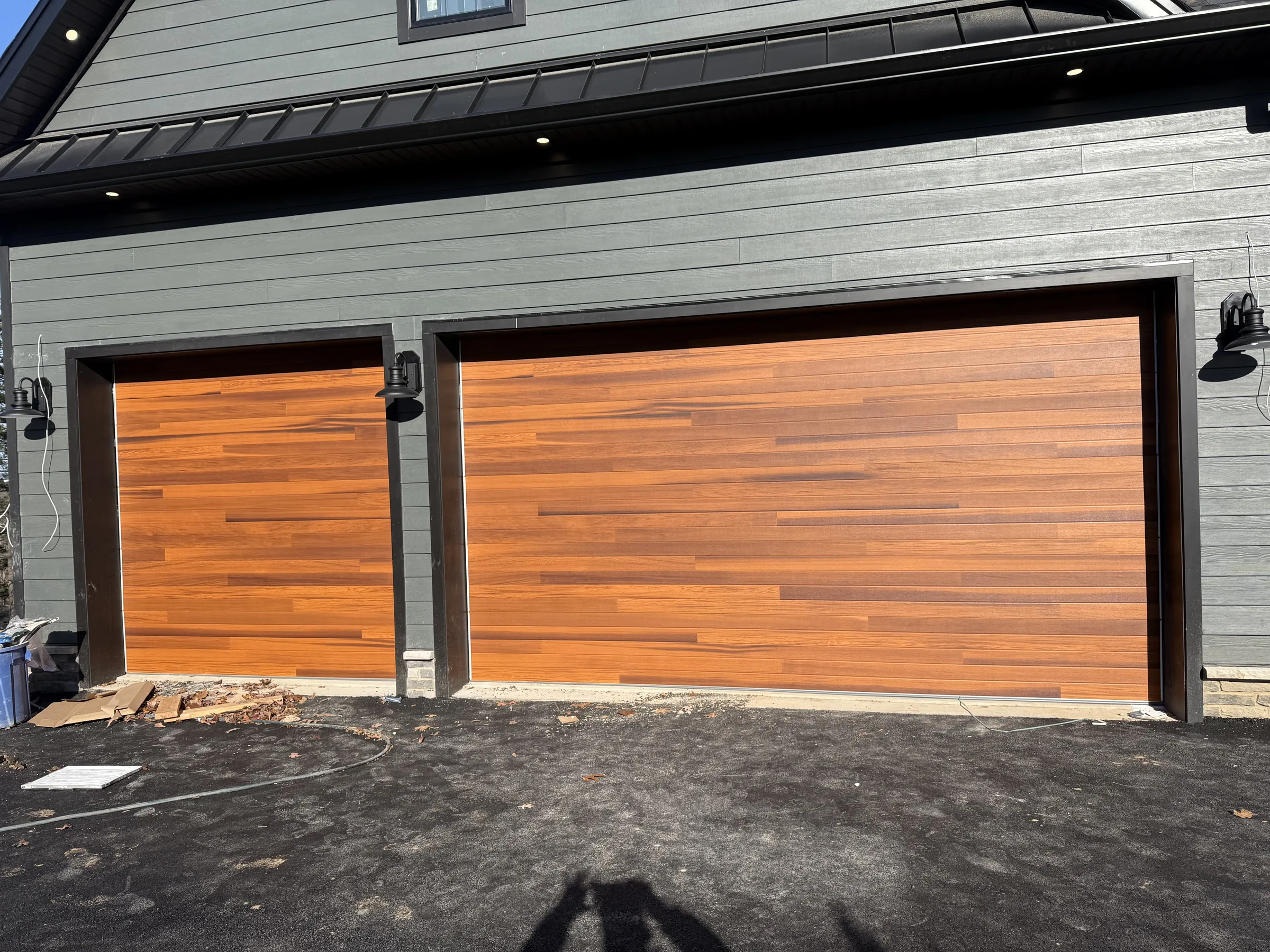 Single and double flush wood-look garage doors installed on a dark gray residential home.
